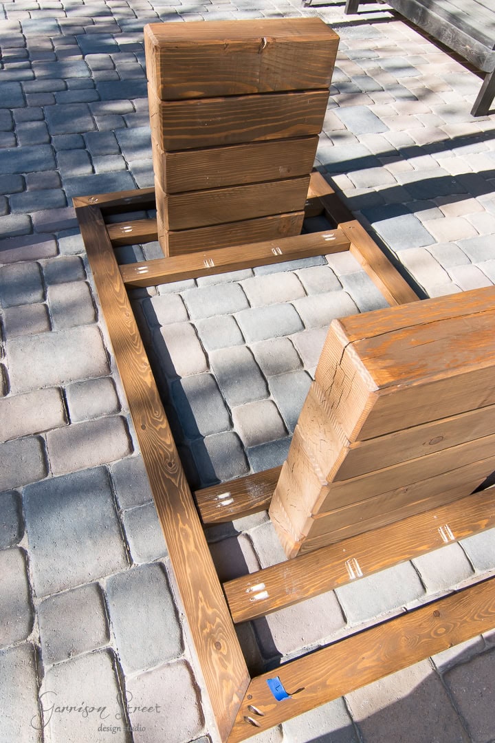 Wooden structure of an unfinished table upside down on a paved outdoor surface. The legs are made of stacked wooden beams.