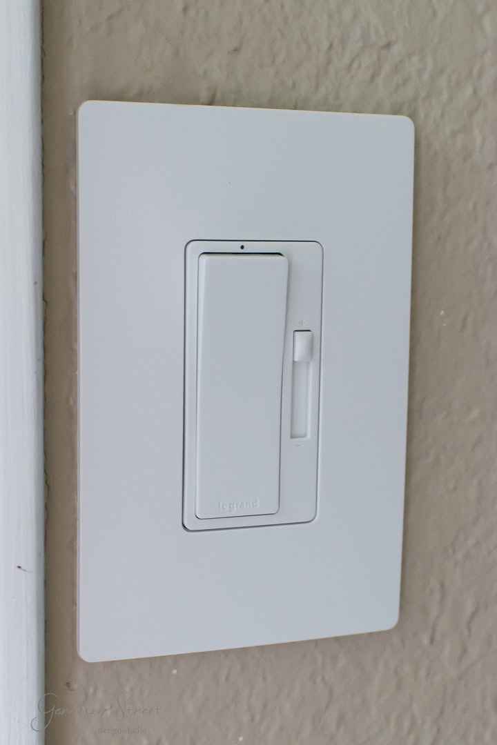Close-up of a white dimmer light switch with a sleek rectangular design against a textured beige wall.