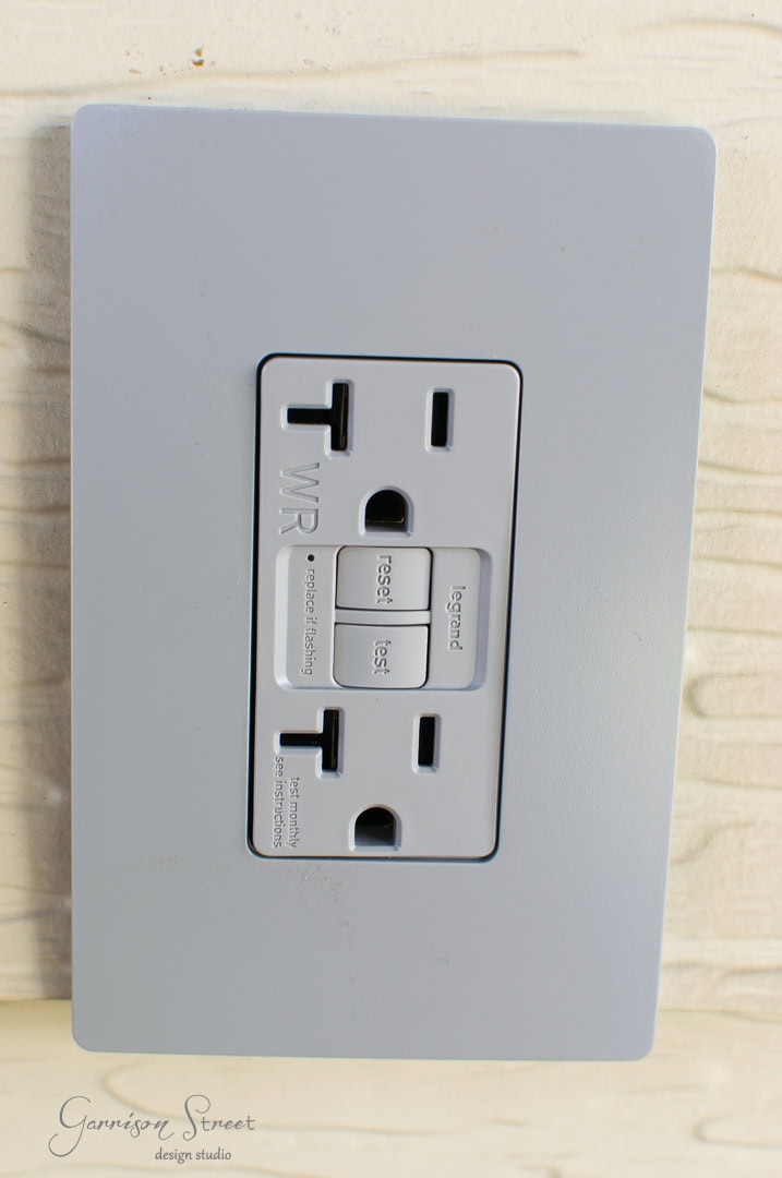 Image of a gray electrical outlet with two standard sockets and two rectangular buttons labeled "reset" and "test". The words "WR" and "Garrison Street Design Studio" are visible on the faceplate.