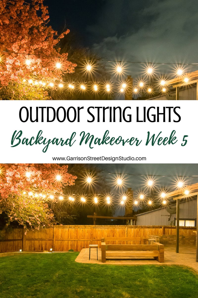 A backyard at night is illuminated with string lights. A large wooden table and benches sit on a patio, surrounded by a wooden fence. Blossoming trees are visible, and text reads, "Outdoor String Lights: Backyard Makeover Week 5.