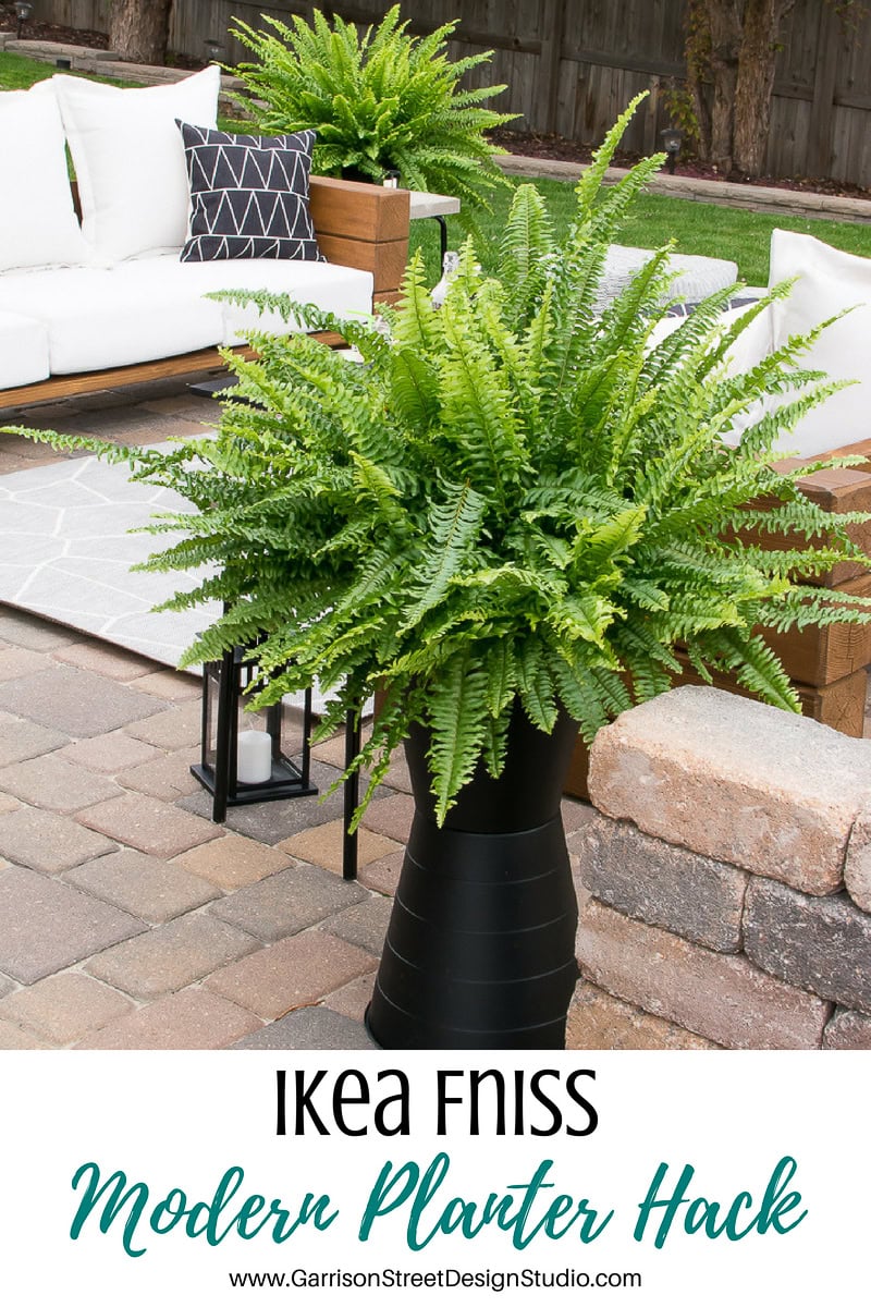 Outdoor patio featuring a large fern in a tall, modern black planter. White sofas with black and white pillows create a chic backdrop. A lantern sits nearby. Text at the bottom reads, "IKEA FNISS Modern Planter Hack.