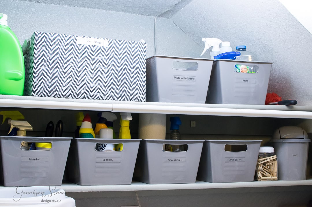 Effortlessly enhance room organization with storage shelves featuring labeled grey bins and a decorative box. The top shelf holds bins for "Floor Protectors" and "Floor", along with cleaning supplies, while the bottom offers tidy sections for "Laundry", "Solutions", "Miscellaneous", and "Shoe Care".