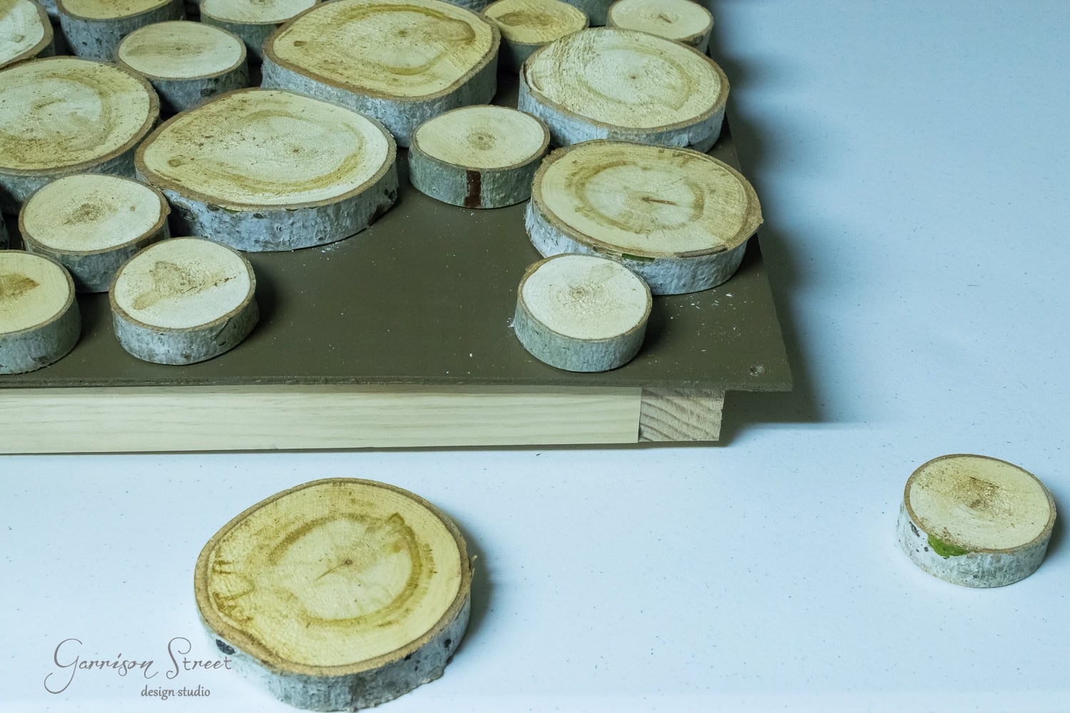 Wood slices of various sizes arranged on a dark board, reminiscent of logs ready for a fireplace insert, with a couple of slices placed on a white surface nearby.