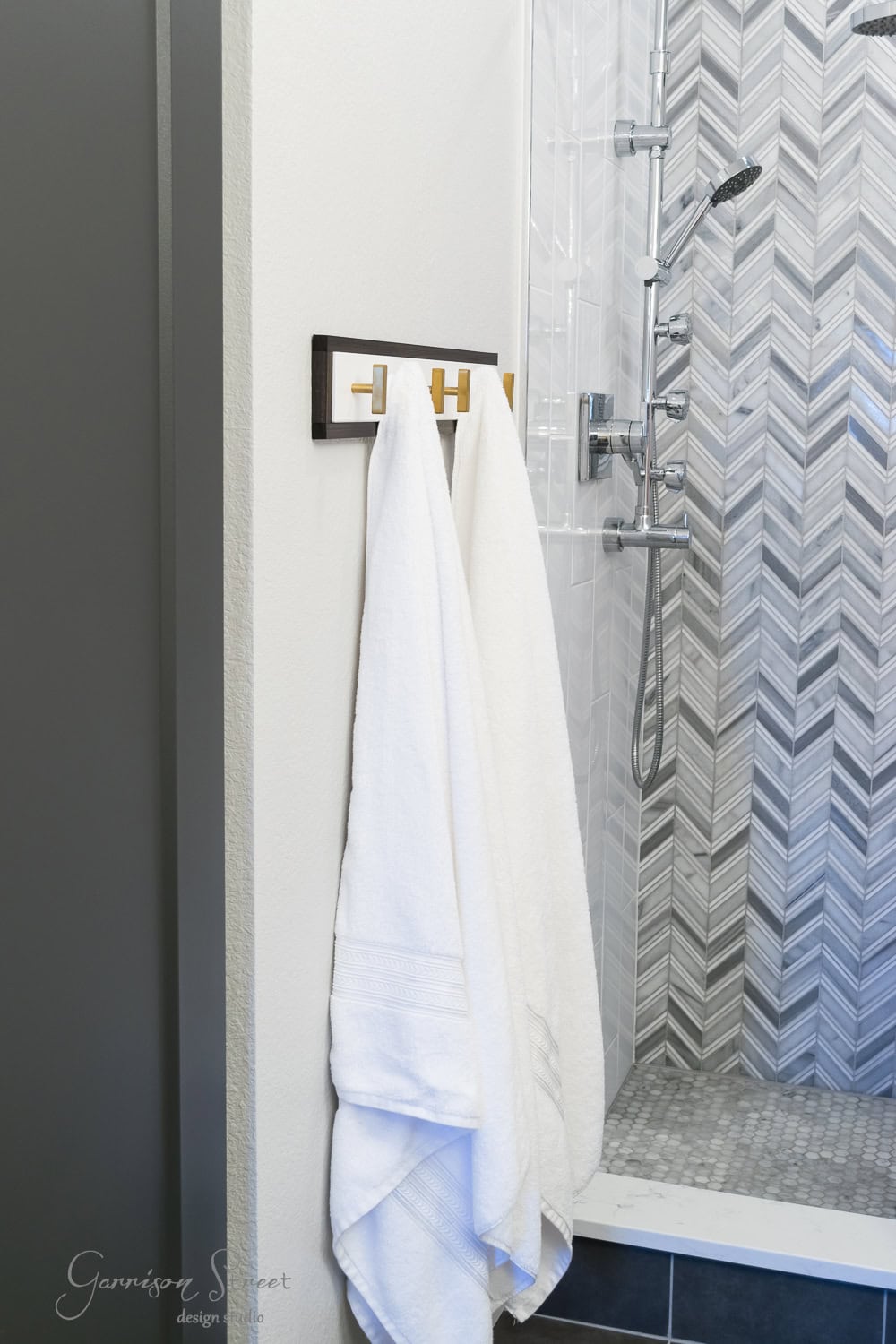 Bathroom with a modern shower featuring herringbone tile walls and a hexagonal tile floor. Outside the shower, two white towels hang neatly on a stylish Ikea towel rack, adding a touch of elegance to the space.
