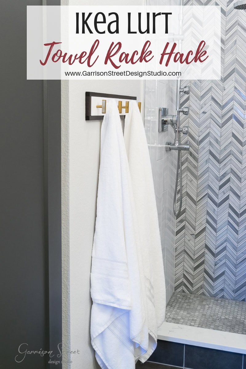 A bathroom featuring a clever towel rack hack using the Ikea Lurt showcases two white towels elegantly hanging on a wooden rack. Mounted on a wall adorned with herringbone-patterned tiles, the design captures a modern and minimalistic essence.