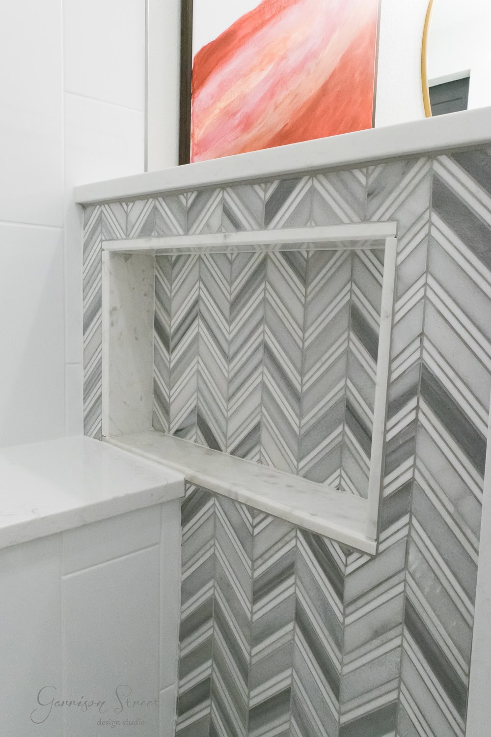 Bathroom wall with elegant gray and white chevron-patterned tiles, featuring a recessed shelf. The chevron pattern adds a modern touch to the space, complementing a nearby pink-hued artwork.