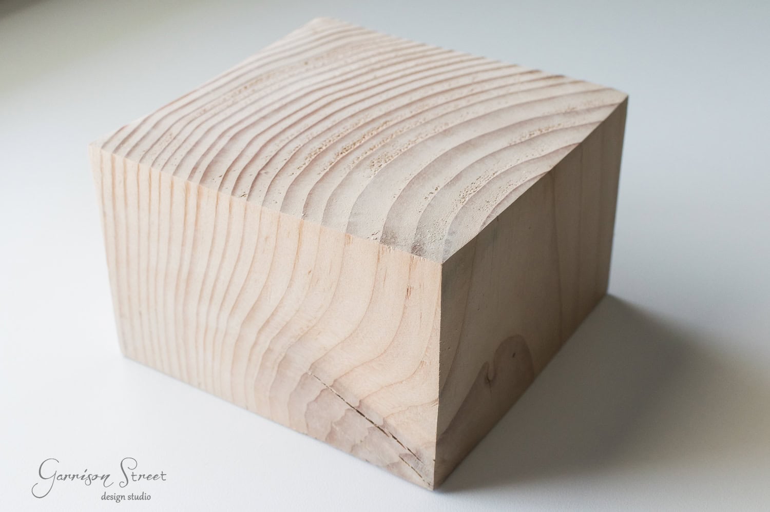 DIY Dollar Store Christmas Tree Hack A close-up of a light-colored wooden block with visible grain patterns and smooth edges, sitting on a white surface. The block appears freshly cut, showcasing natural wood textures.