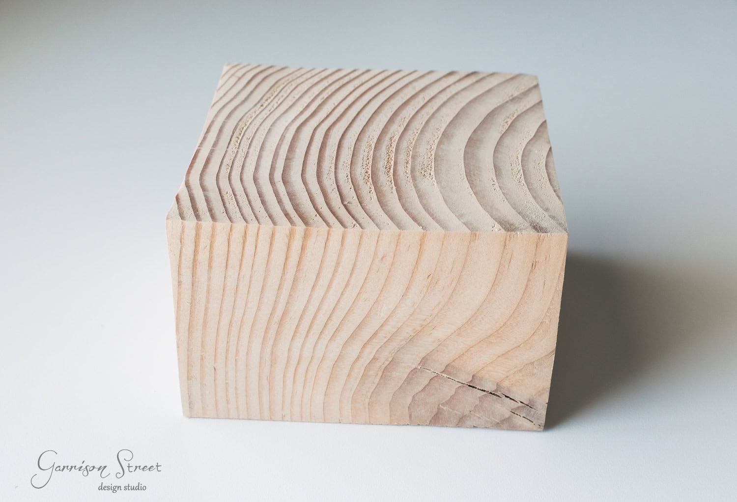 DIY Dollar Store Christmas Tree Hack A cube-shaped piece of wood with visible grain patterns on a plain background. The wood has a natural, unfinished appearance, showcasing various shades and textures.