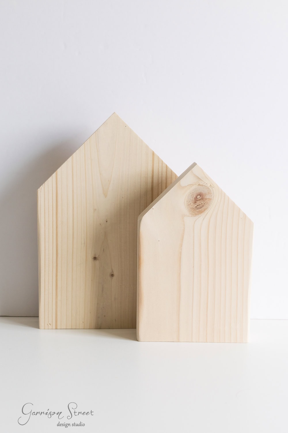 Two wooden house-shaped blocks with smooth surfaces, one slightly taller than the other, placed against a plain white background.