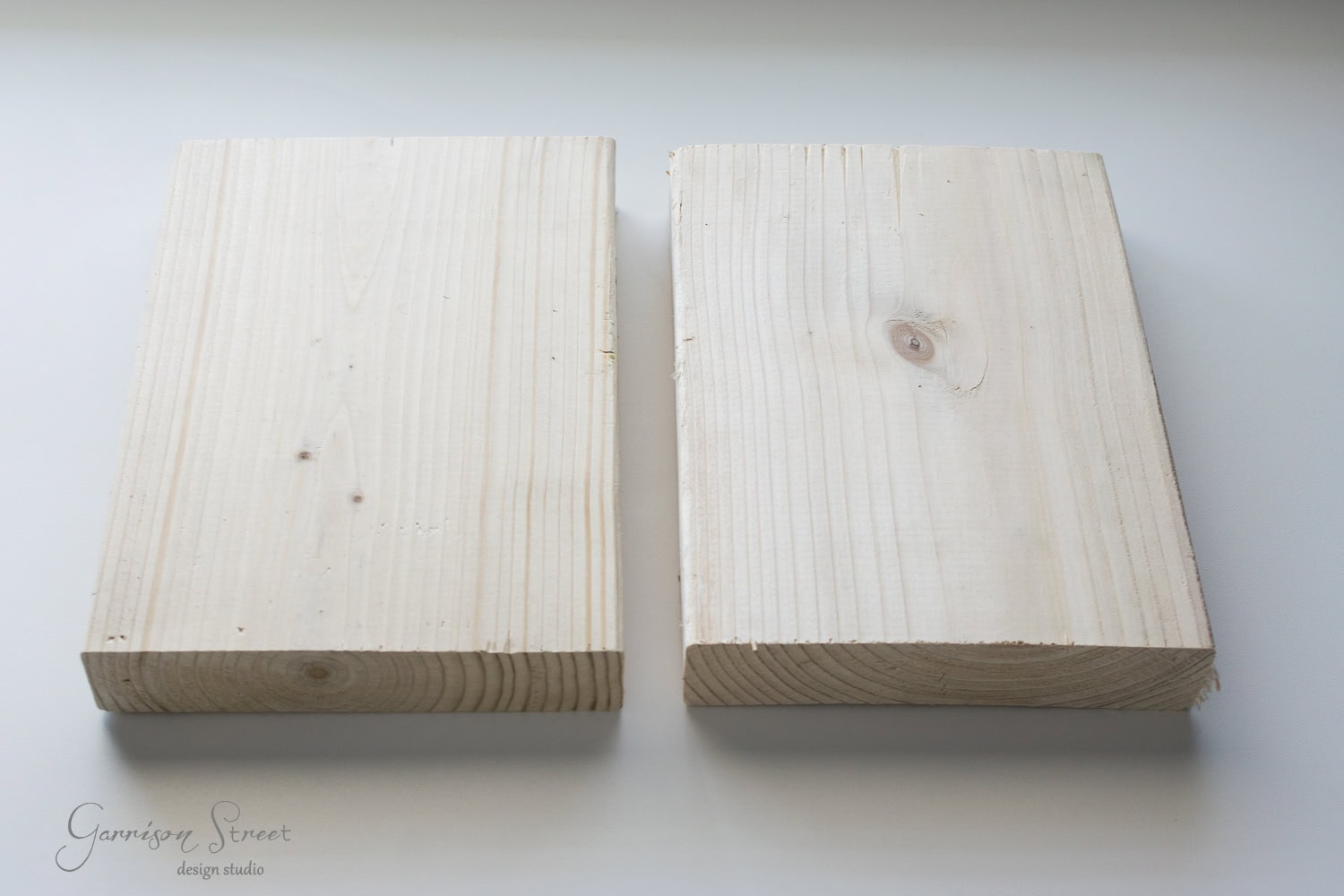Two rectangular pieces of unfinished wood placed side by side on a light surface. The wood has visible grain patterns and a knot on the right piece. The left piece is slightly smoother, with cleaner edges.