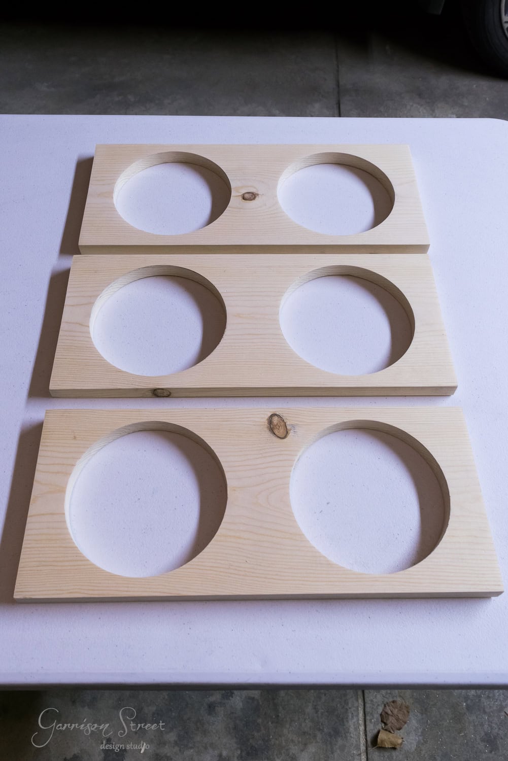 Three rectangular wooden boards with raised circular cutouts sit on a white surface. Each board features two large circular holes in the center, perfect for holding a pet's bowl. The boards boast a smooth finish and natural wood texture.