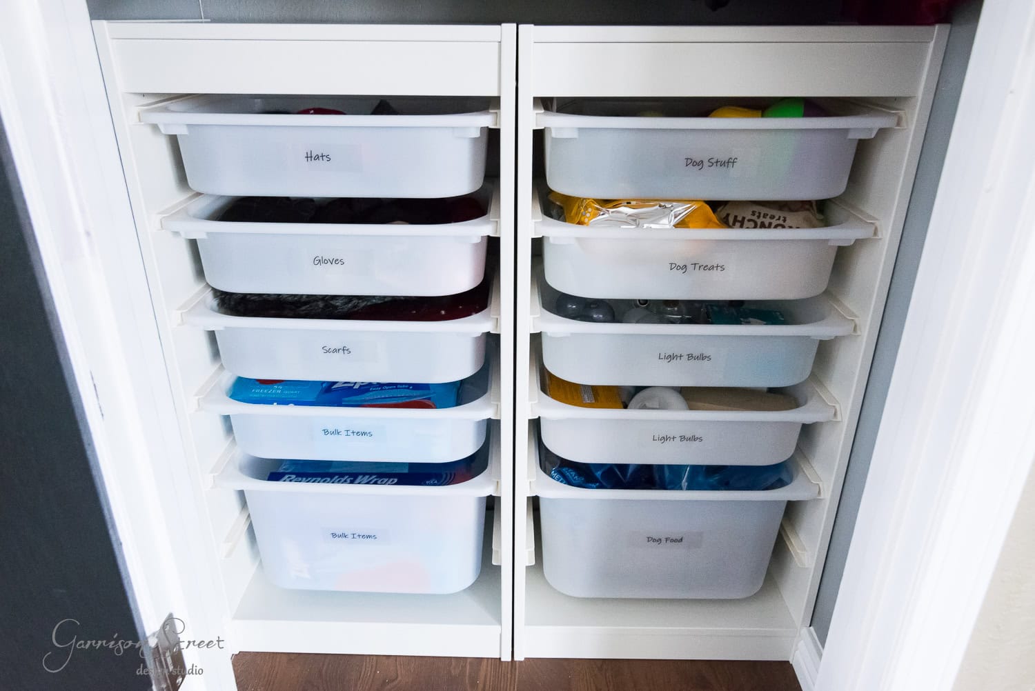 A neatly organized closet features labeled Trofast pull-out bins. The setup includes sections for hats, gloves, scarves, and tote bags on the left. On the right, there are bins for dog supplies, treats, light bulbs, and food to ensure seamless organization in your space.