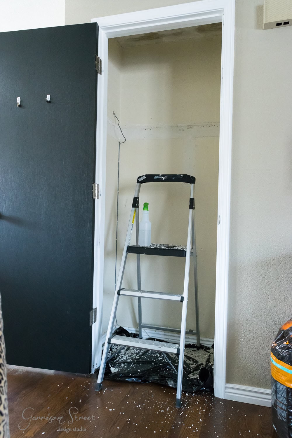 A small IKEA closet converted into a home project space with a step ladder inside. The paint-splattered floor and walls tell tales of creativity, while a spray bottle rests on one of the ladder steps, reminiscent of industrious afternoons spent crafting and organizing.