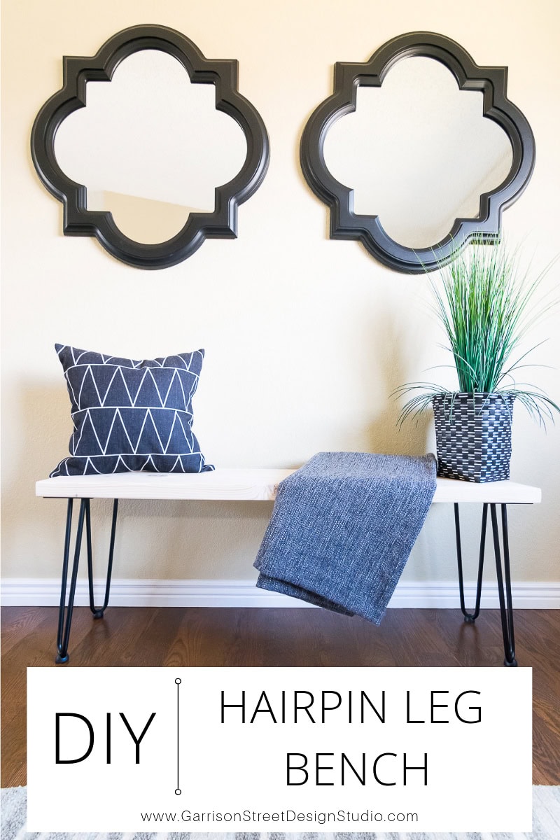 A modern DIY hairpin leg bench with a geometric cushion and blue throw, placed below two decorative mirrors on a beige wall, captures the essence of Garrison Street Design Studio. A potted plant adorns the bench, adding a touch of nature to the contemporary scene.