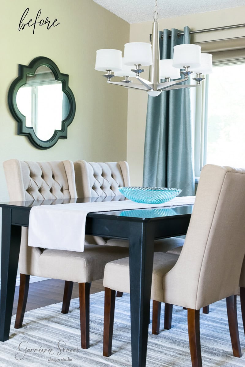 A dining room featuring the best dark wooden table, beige upholstered chairs, and a stunning silver chandelier. Gray curtains hang elegantly on the wall next to a decorative mirror. A textured bowl rests atop a white runner on the table.