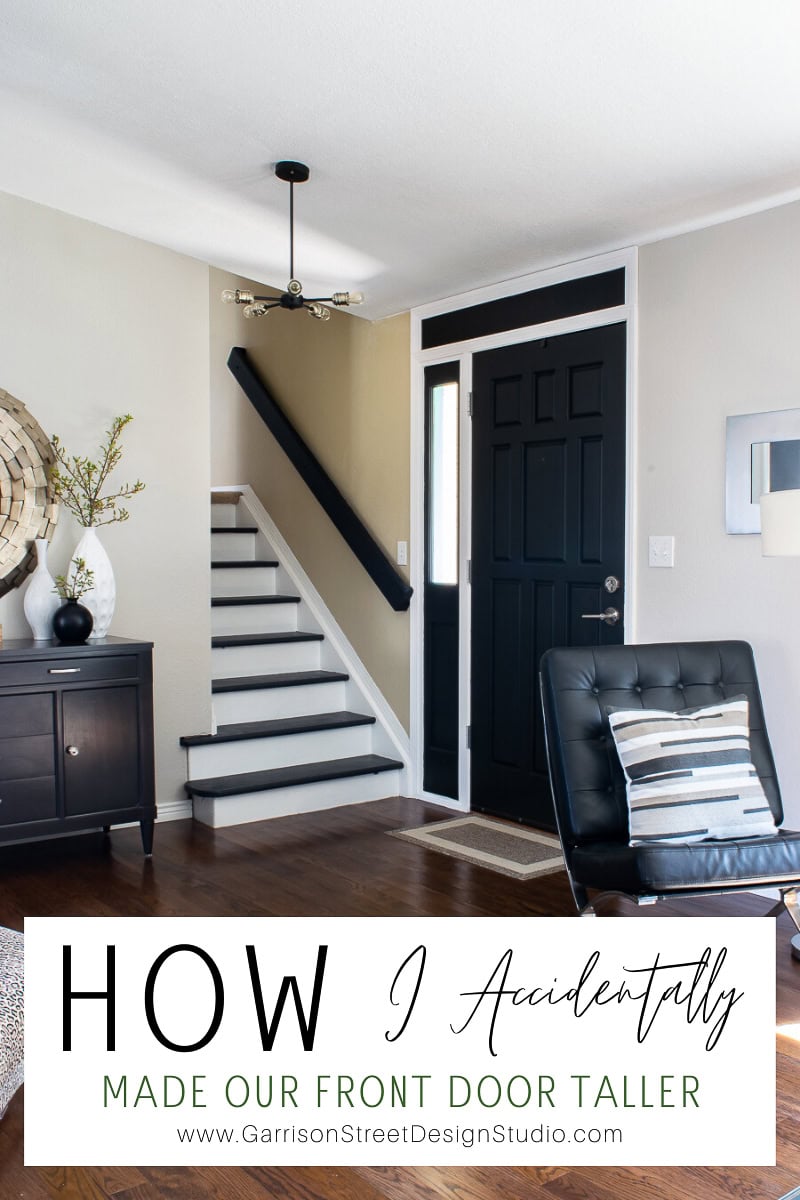 Modern living room entryway with a sleek front door, white walls, and dark wood flooring. A black leather chair with a striped pillow sits in the foreground, beneath a staircase. Decorative plants and a cabinet grace the left side. Text overlay reads "How I Accidentally Made Our Front Door Taller.