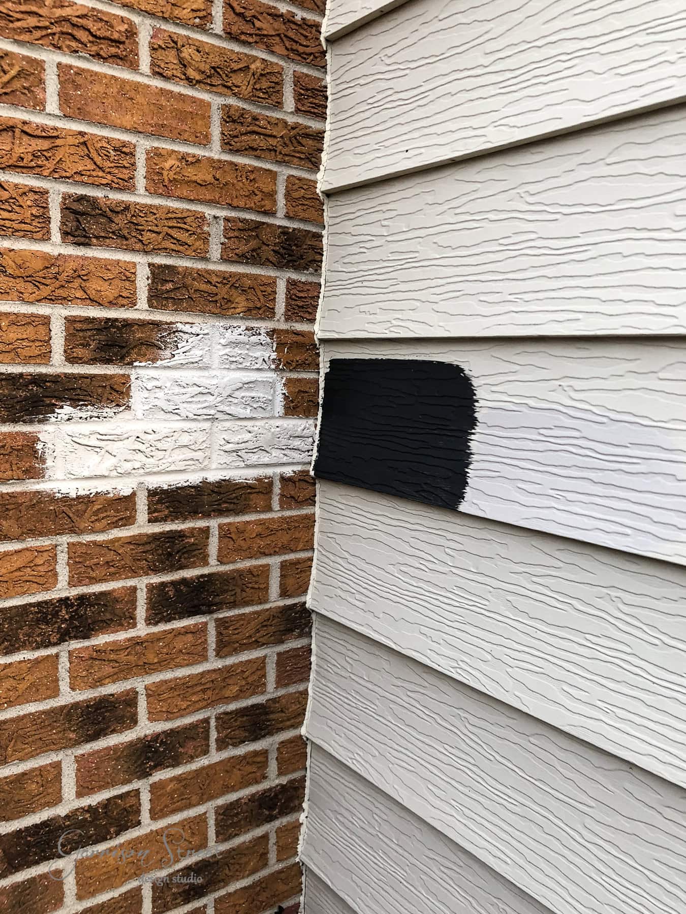 A corner of a building showcases contrasting surfaces: one side flaunts textured red bricks, partially painted white, while the other features cream-colored siding adorned with vertical black and white paint samples.