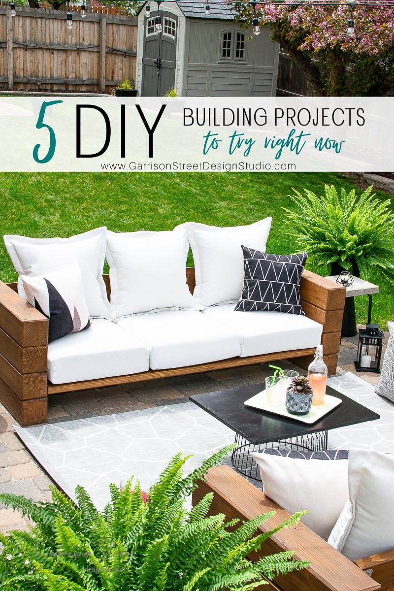 Outdoor patio with a white cushioned wooden sofa, decorative pillows, a small table adorned with potted plants, and lush green ferns. Text overlay reads, "5 DIY Building Projects to Try Right Now" from Garrison Street Design Studio.