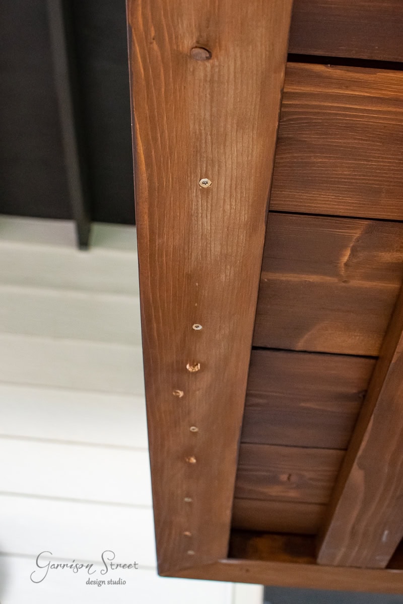 Close-up view of a wooden ceiling with a polished finish and visible screws. The image features a blend of dark and light wood tones, displaying intricate details of the wood grain.