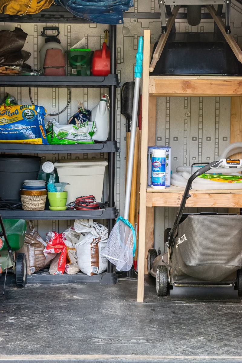 A neatly organized garage showcases shelves filled with gardening supplies, seed bags, and tools, epitomizing DIY organization. A lawn mower sits on the floor while pool cleaning equipment leans against the shelves. Pots and plant-related items suggest a focus on outdoor maintenance.