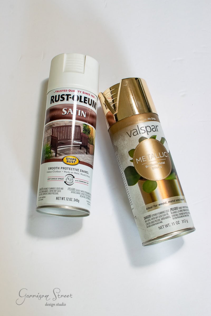 Two spray paint cans on a white surface: one Rust-Oleum Satin spray can with a wooden chair image, perfect for your fall DIY projects, and a Valspar Metallic spray can with a gold top. The background features a "Garrison Street Design Studio" watermark.