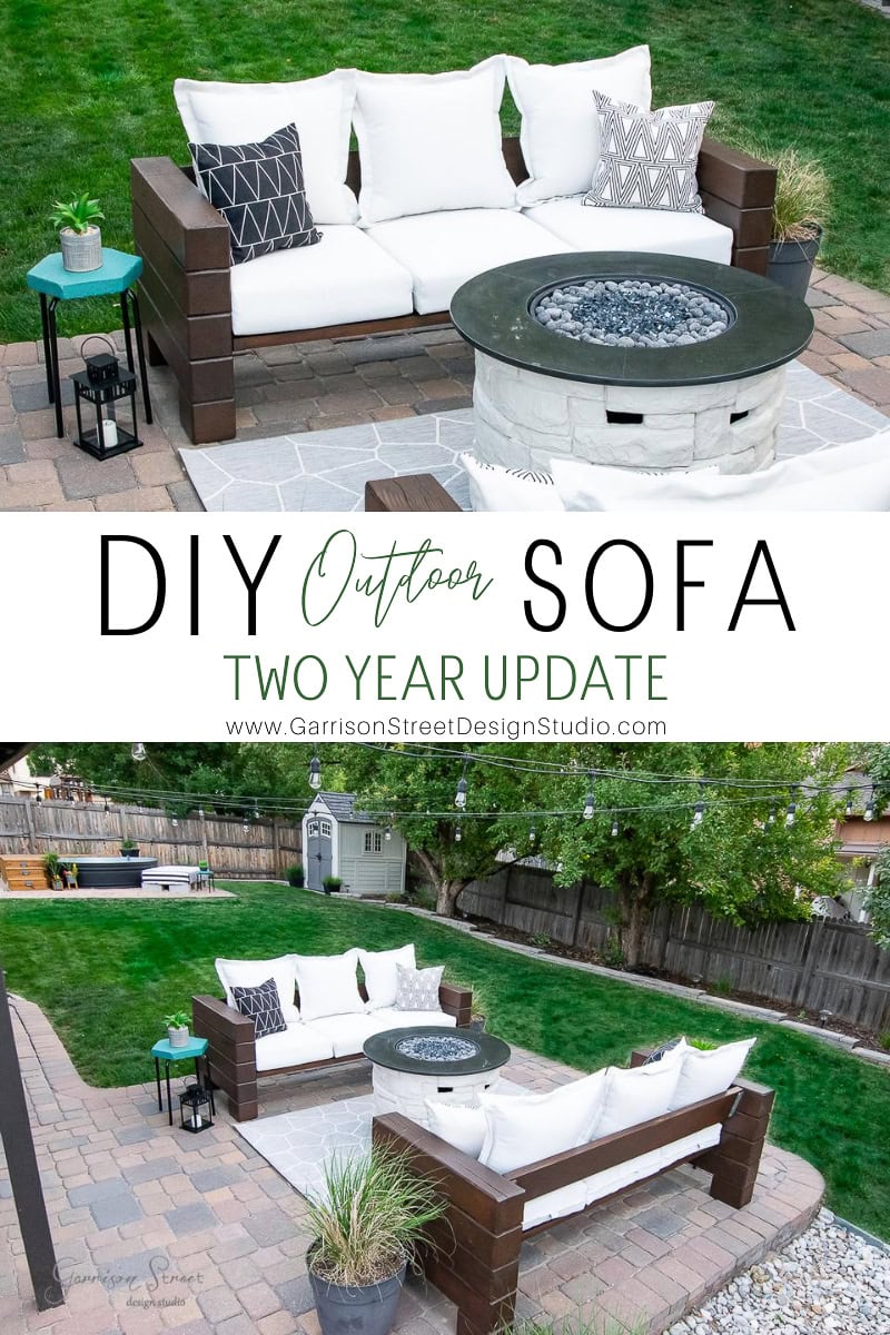 Outdoor patio featuring a stylish DIY outdoor sofa crafted from dark wood with white cushions encircling a circular fire pit. A small green side table holds a plant, adding charm to the paved area. In the background, a lush grass yard is enclosed by a wooden fence.
