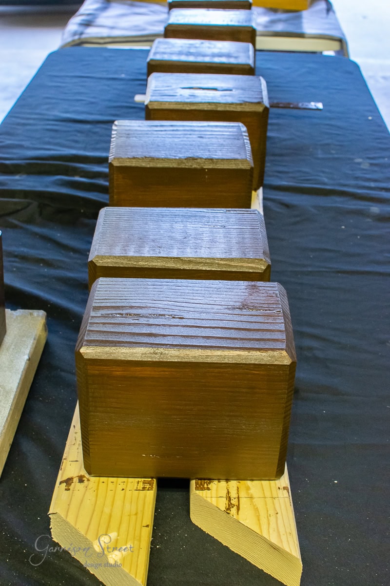 Close-up of wooden blocks lined up on parallel support beams, reminiscent of the sleek lines found in an outdoor sofa design. The blocks have a smooth, glossy finish and rest elegantly on a black surface, each perfectly aligned on the wooden planks beneath them.
