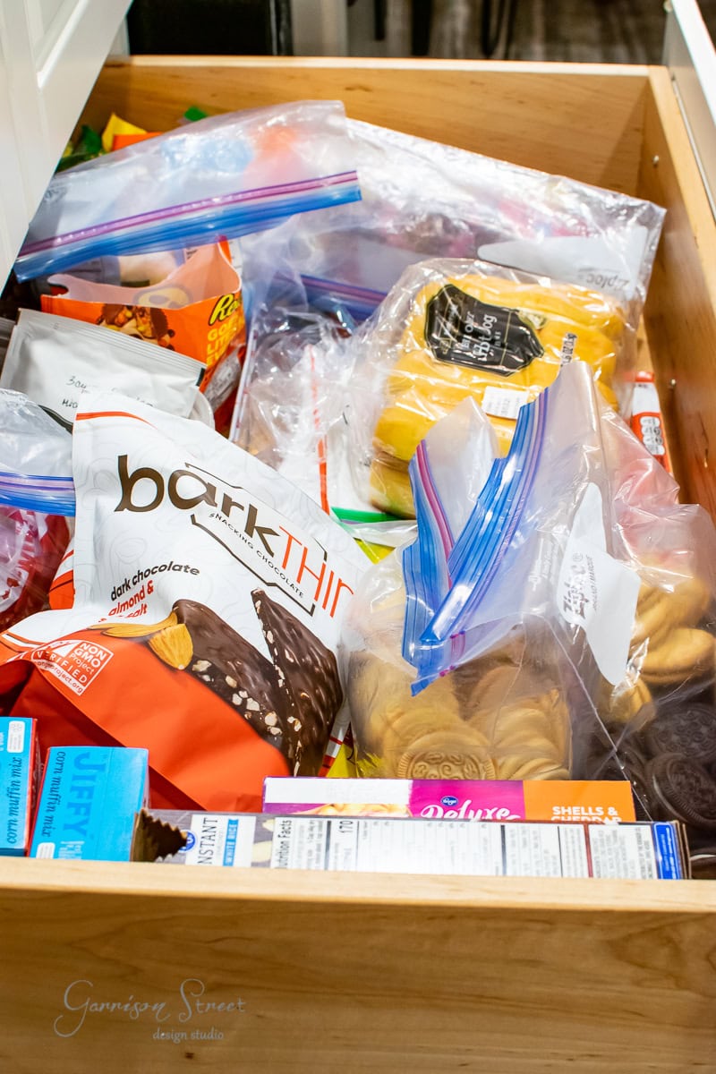 A well-organized drawer filled with various snacks in resealable bags and packages, including chocolate bark, Reese's, Ritz crackers, and other assorted treats—a mini pantry in your cabinet.