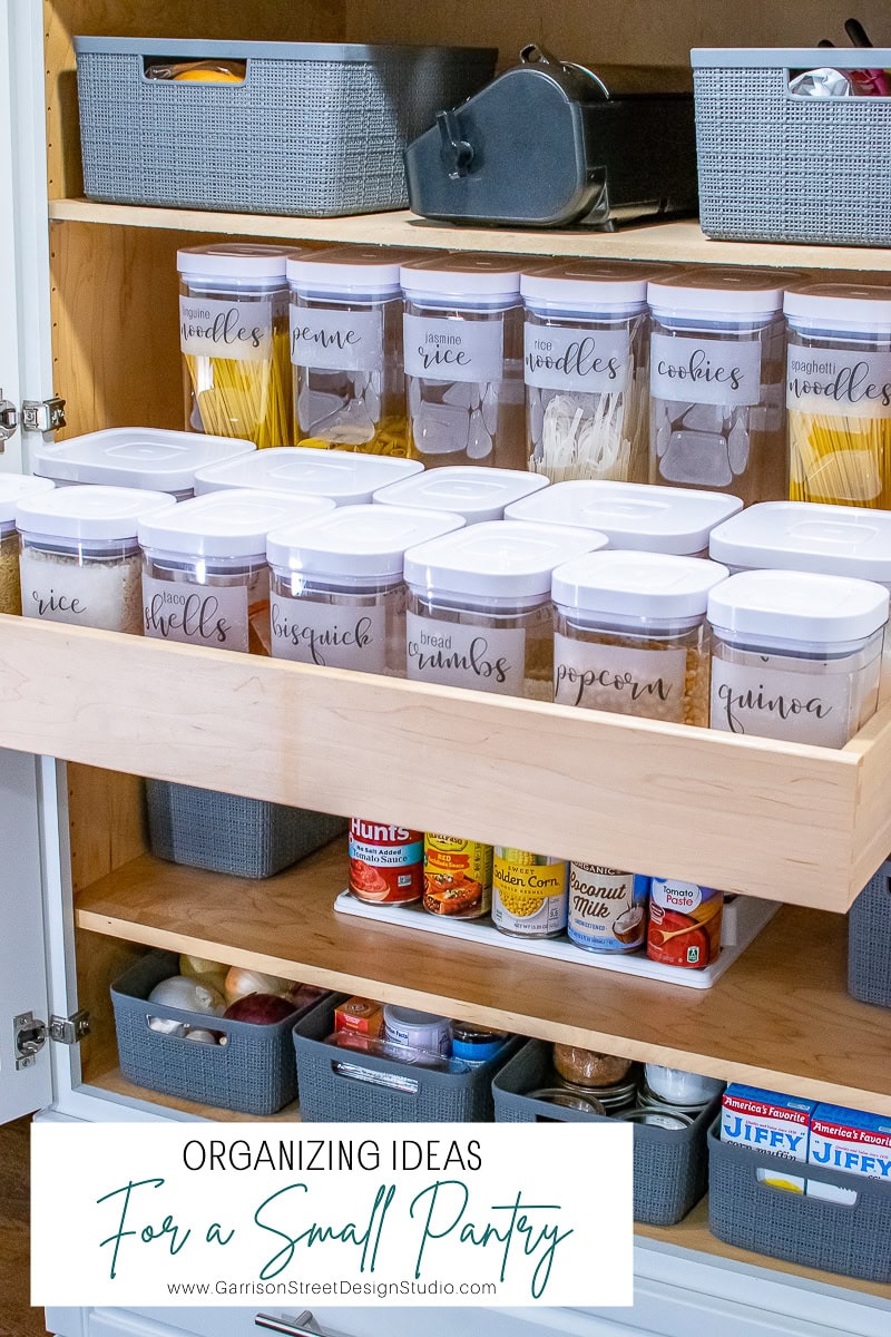 A small pantry boasts impeccable organization, with neatly arranged shelves featuring labeled containers of pasta, rice, and more. Transparent with white lids, these containers sit alongside gray baskets that enhance the cabinet's efficient storage solutions.