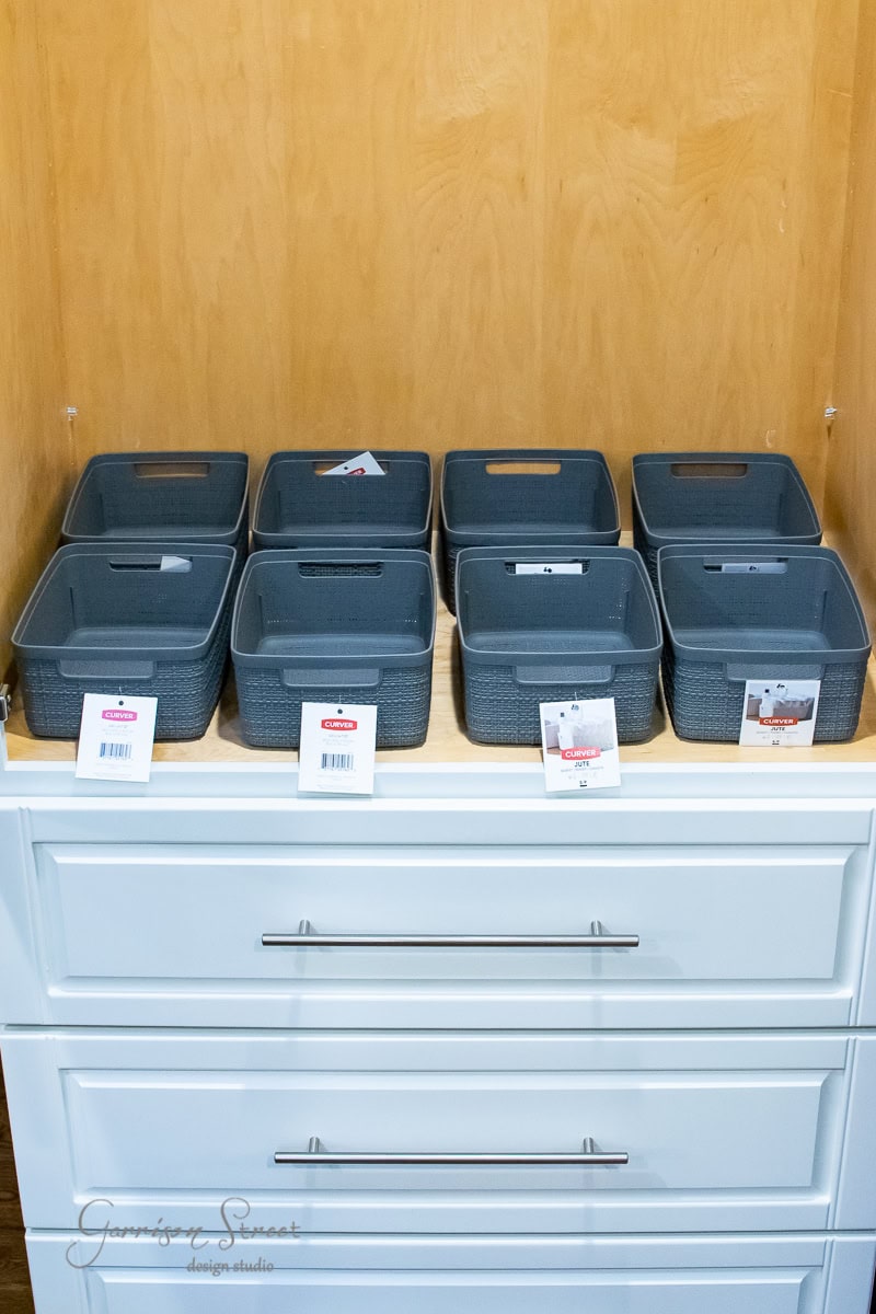 This organizational cabinet features two white drawers and nine gray storage bins, each thoughtfully labeled with tags. Ideal for streamlining your pantry, its interior boasts a light wood finish that complements any decor.