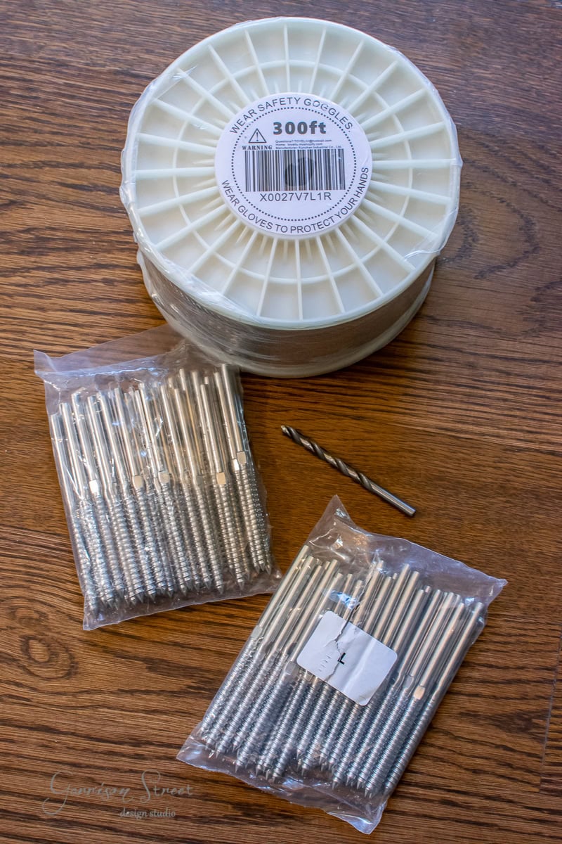 A flat lay image showcases a spool of 300 ft cable, a drill bit, and two bags of screws on a wooden surface, perfect for your next DIY project.