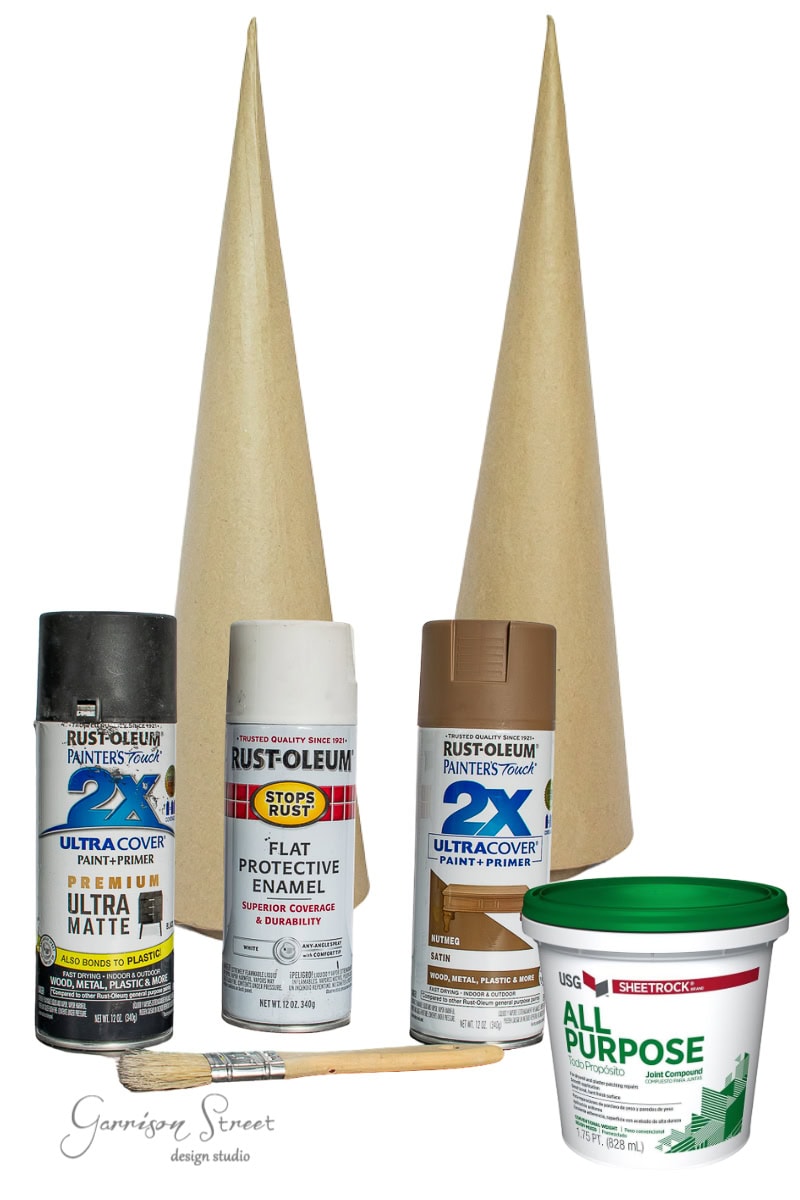 Craft supplies for a project: two paper cone forms to mimic Christmas trees, white and metallic spray paints, a can of all-purpose joint compound, and a wooden dowel—all elegantly arranged in a vertical composition for your festive fottery.