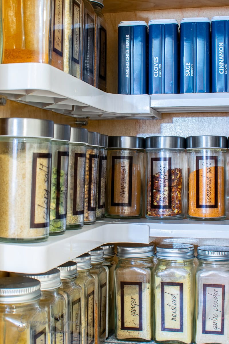A well-organized spice cabinet features labeled jars and containers. The shelves hold a variety of spices, including paprika, cumin, mustard, sage, and cinnamon. This efficient setup showcases the art of spice organization with neatly aligned jars for easy access.