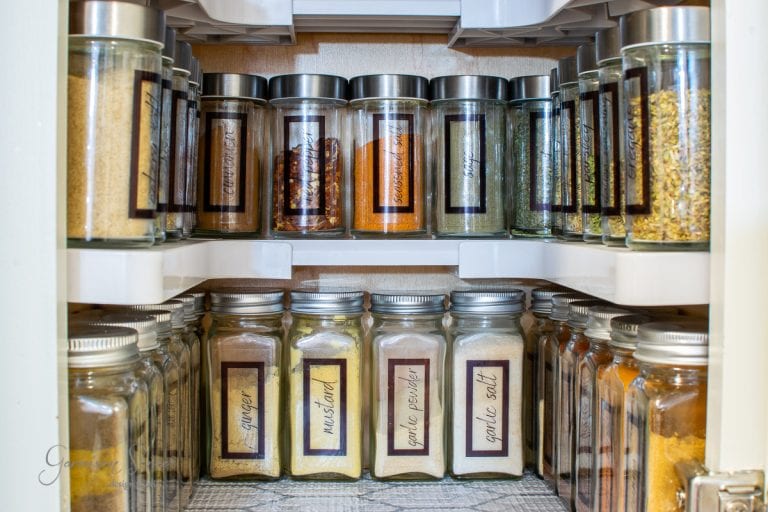 A neatly organized spice cabinet showcases glass jars of various spices. The labeled jars, featuring ginger, mustard, white pepper, and garlic salt, are arranged with precision on rotating shelves for optimal organization.