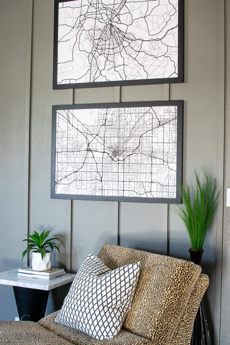 The room features two framed map prints as DIY art on the wall, a leopard print sofa adorned with decorative pillows, and a small table hosting lush potted plants.