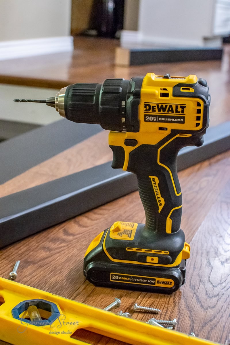 A yellow and black cordless Dewalt drill, perfect for your next DIY project, stands upright on a wooden floor. With its 20V MAX brushless technology, it's ready to tackle tasks like installing cable railing, complete with visible screws and a black metal frame nearby.