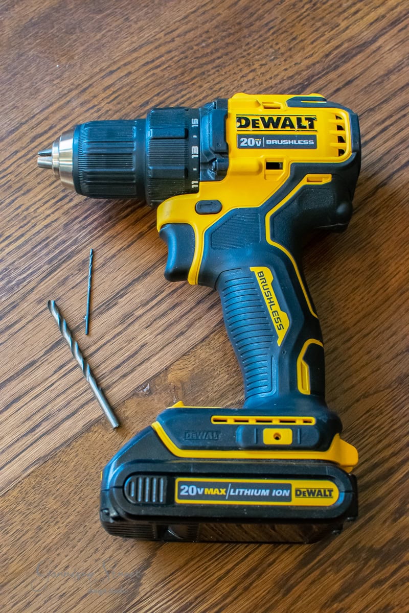 A yellow and black cordless power drill rests on a wooden surface, ideal for any DIY project, accompanied by two drill bits. The drill is labeled with "DEWALT" and "20V Lithium Ion," perfect for tasks like installing cable railing with precision and ease.