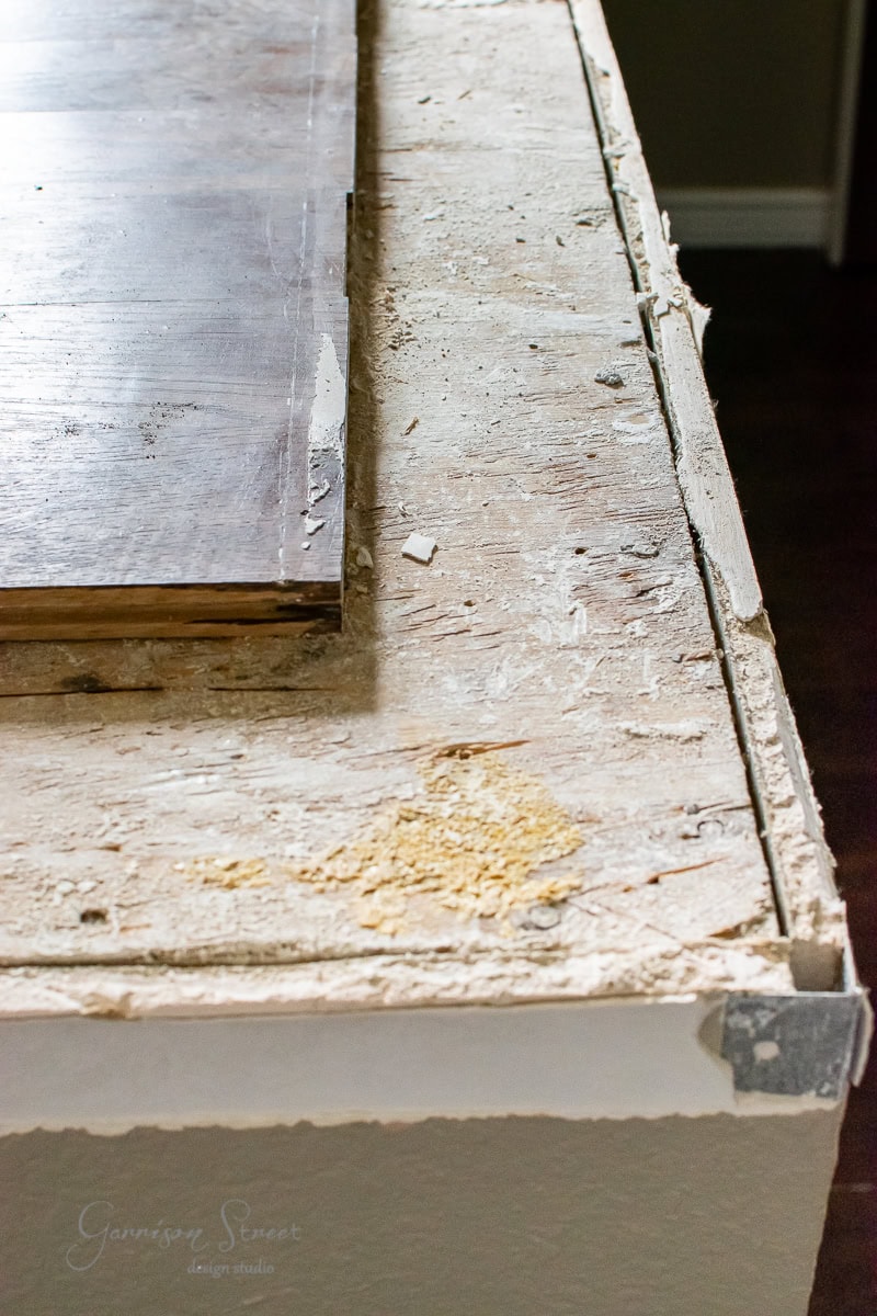 A close-up of a DIY countertop renovation in progress reveals a worn and chipped surface with exposed wood and drywall. Pieces of plaster and dust are scattered around, mirroring the industrious vibe seen in cable railing projects, indicating active remodeling work.