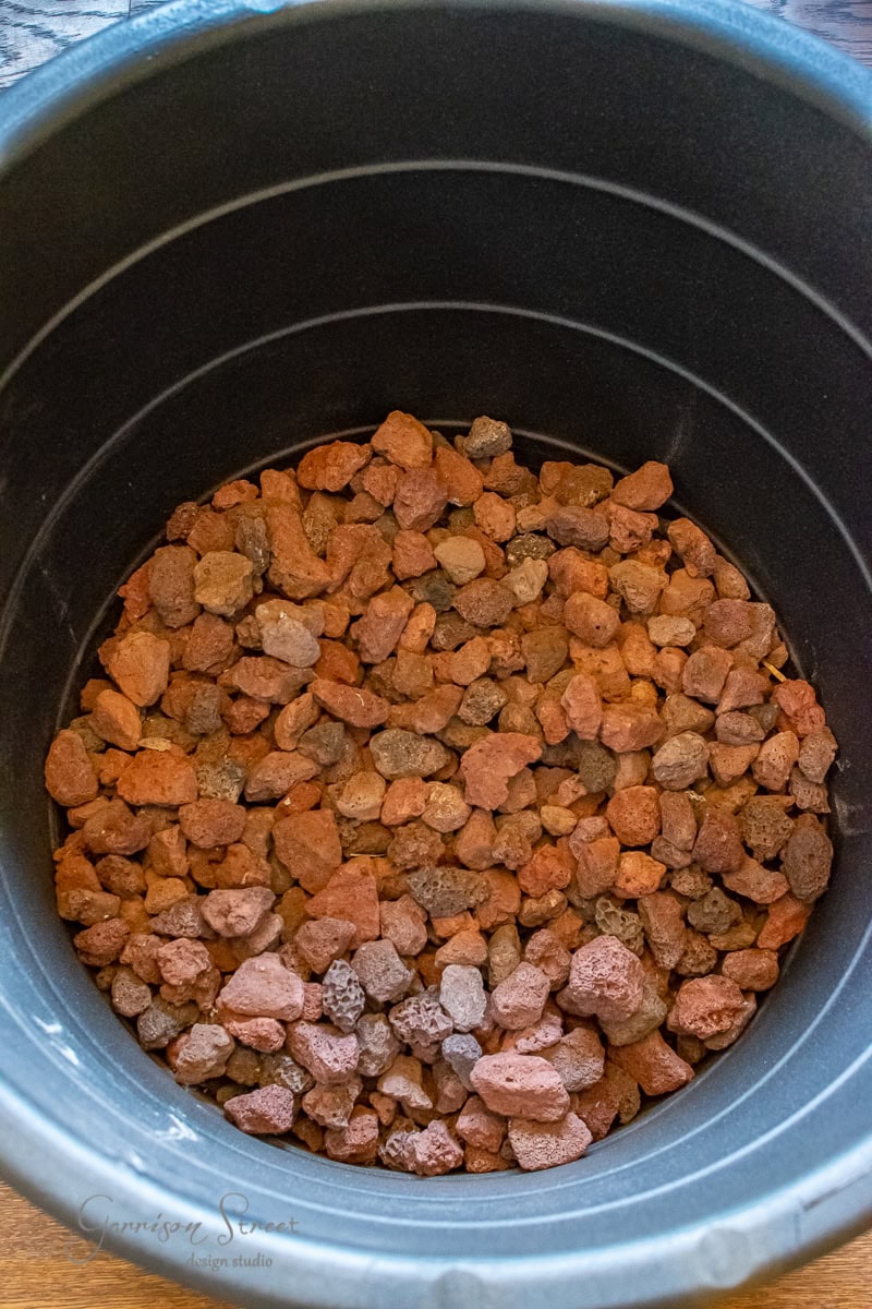 A large black plastic planter brimming with a layer of reddish-brown lava rocks makes for an ideal DIY gardening project.