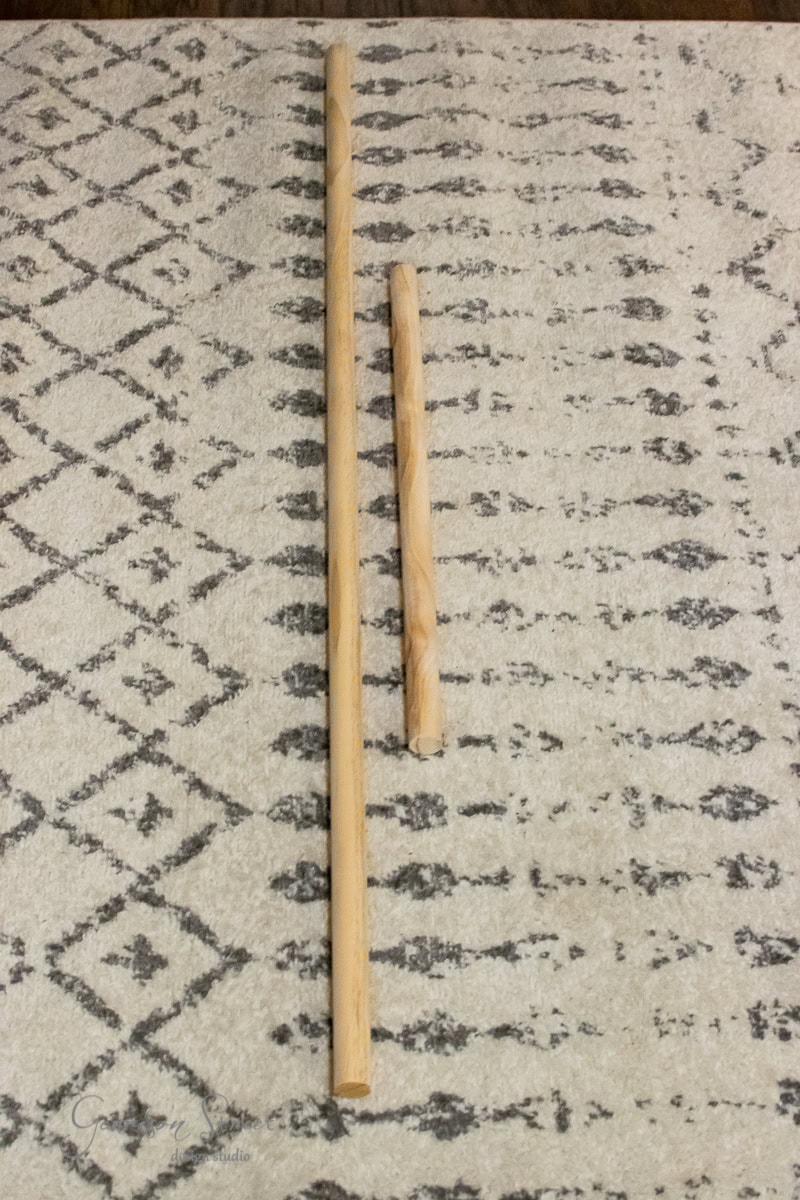 Two wooden sticks of differing lengths are placed parallel on a patterned, textured carpet. The larger stick is roughly twice the length of the smaller one.