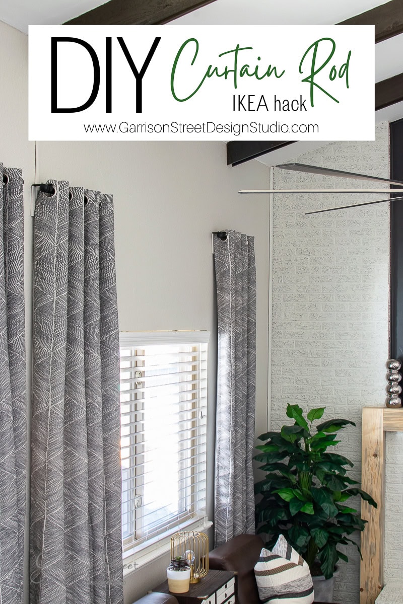 Photo of a cozy living room corner featuring stylish gray patterned curtains on a clever DIY curtain rod from IKEA. A lush green plant complements the wooden table adorned with decorative items. Overhead, a text banner: "DIY Curtain Rod IKEA Hack www.garrisonstreetdesignstudio.com."