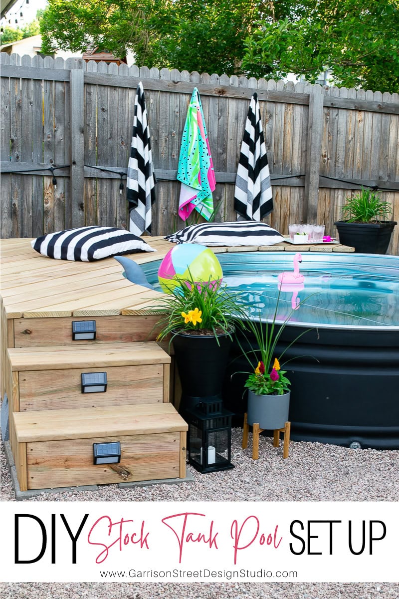 A stock tank pool with a wooden deck and steps graces the backyard. Towels hang on a wooden fence, while nearby plants, pool accessories, and a lantern complete the scene. Text reads, "DIY Stock Tank Pool Set Up," with a website link included.