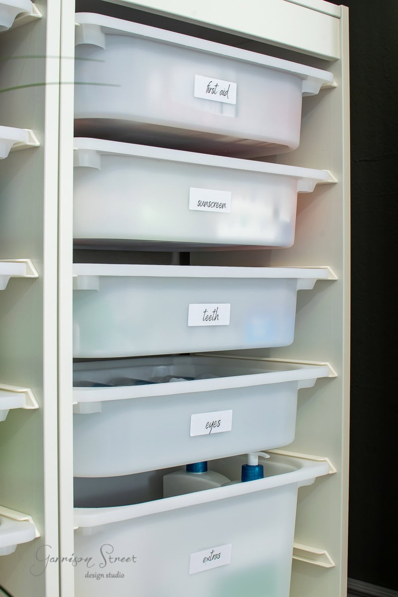 A white storage unit stands proudly, a result of a recent linen closet makeover. It features five labeled plastic drawers: "first aid," "sunscreen," "teeth," "eyes," and "extras." Through the translucent fronts, some essentials peek out, ready to serve.