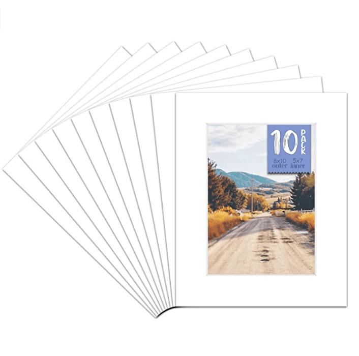 A stack of ten white photo mats, each with a 5x7 opening, creates the perfect picture frame for an image of a rural dirt road lined with trees under a clear sky. "10 Pack" is subtly displayed on the oversized mat at the front, adding a touch of elegance to any photograph.