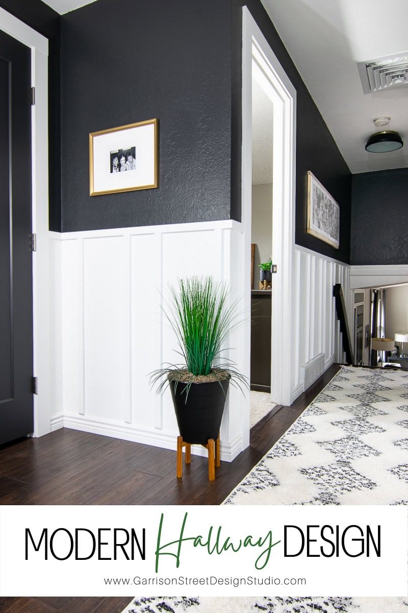 Modern hallway with dark walls and white board and batten wainscoting. A framed photo hangs above a green plant in a black pot. A patterned rug runs along the dark wooden floor. Text overlay reads "Modern Hallway Design" with a website link beneath.