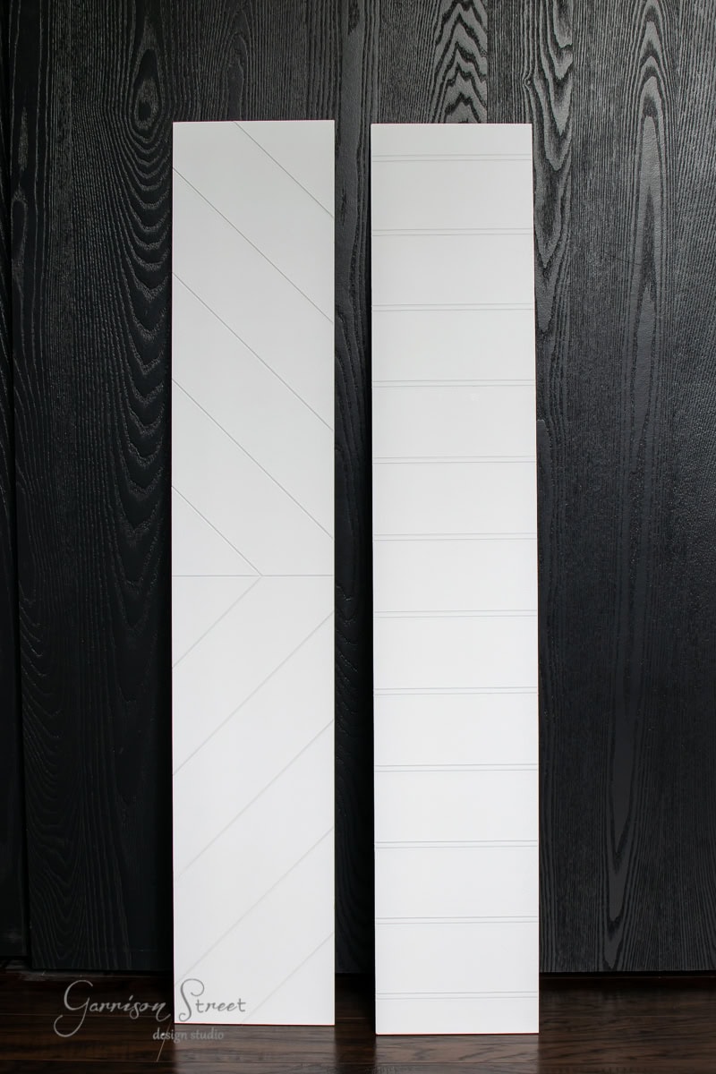 Two tall white wooden boards stand against a dark wood-textured wall, resembling stair treads. The board on the left showcases a chevron pattern, while the board on the right features horizontal lines.