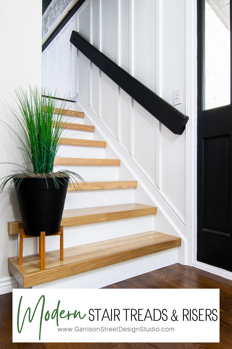 A modern interior staircase features sleek stair treads with wooden finishes and crisp white risers. A black handrail runs along the wall, while a potted plant adorns the bottom step. The wall below boasts elegant paneling. Text reads, "Modern Stair Treads & Risers.