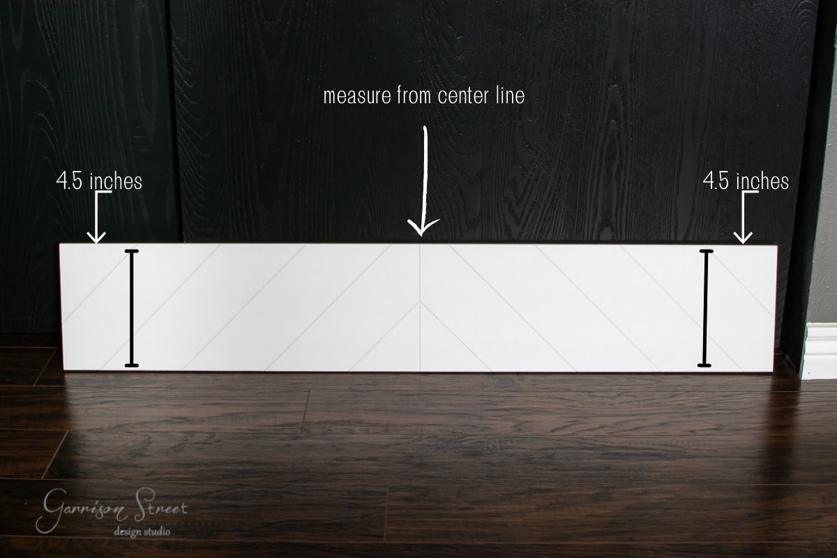 A white board with black lines rests on a dark wood floor, resembling stair treads. Arrows and text indicate measuring 4.5 inches from each side and from the center line.