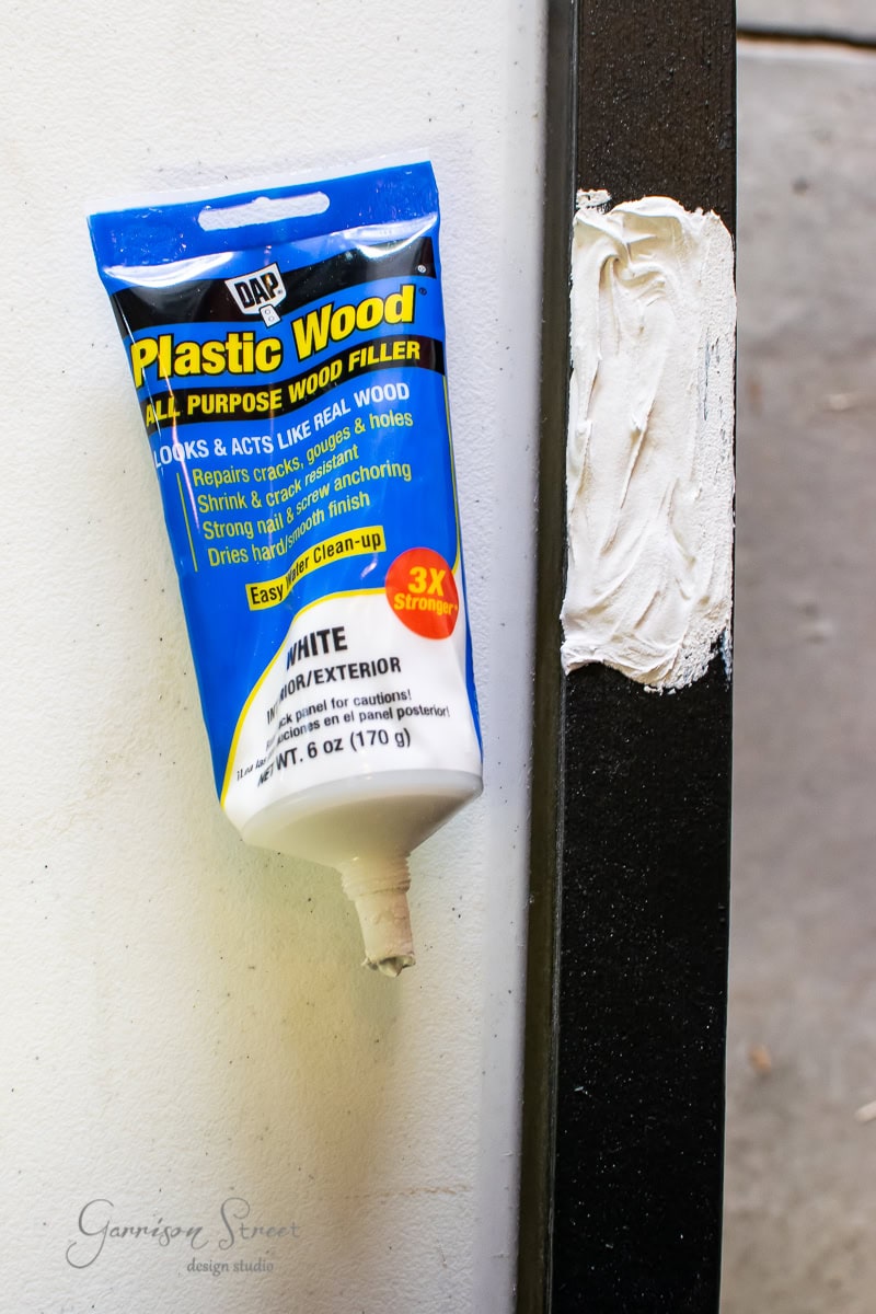A tube of DAP Plastic Wood All Purpose Wood Filler in white is displayed vertically with some filler applied. The tube is partially squeezed, showing the cap off.