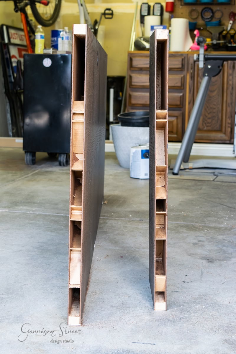 In a garage workshop filled with tools and cabinets, two hollow wood doors stand side by side. One towers over the other, showing their internal structure.